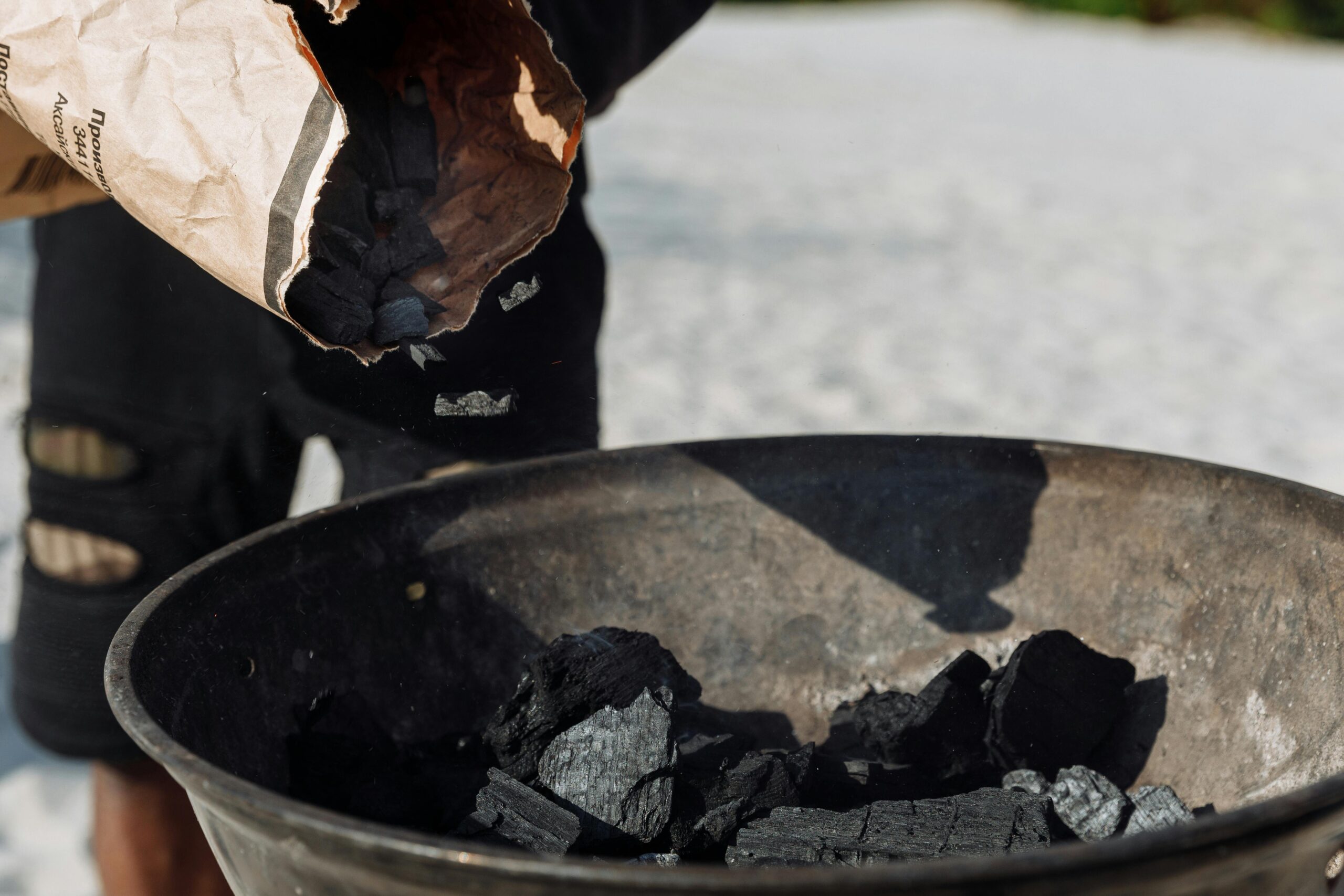 Detailed image of charcoal poured from a bag into a grilling basin outdoors.